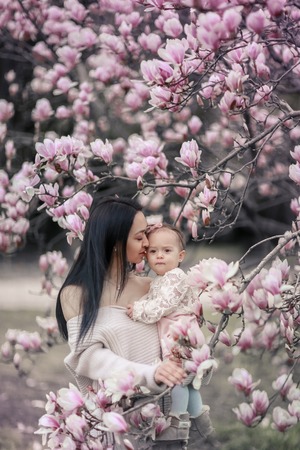 Cute Baby 6 month old Girl in Pink Outfit with Big Blue Eyes with Young Beautiful Mother at Spring,...