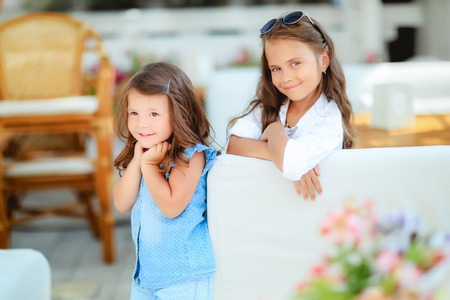 Two cute little girls standing in jumpers and sun glasses on the terrace background in the studio. Summer, fun, family and vacations concept. Two fashion sisters posingの写真素材