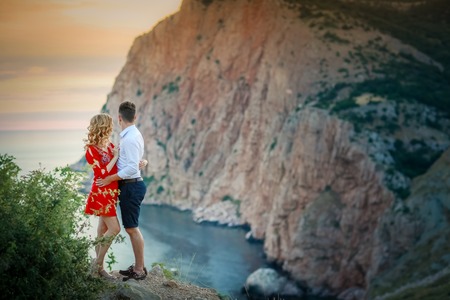Happy young family pregnant pretty girl with husband on the cliff in mountains over sunset lights.の写真素材