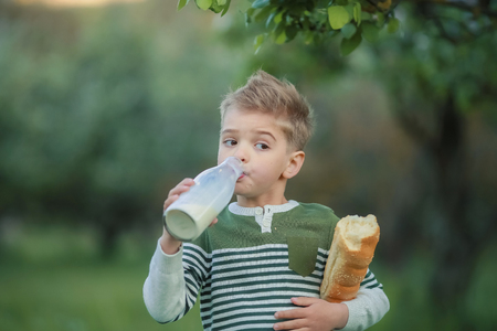 Little boy with girl drink milk and eat a loaf of bread on a haystack in a village at sunset.の写真素材