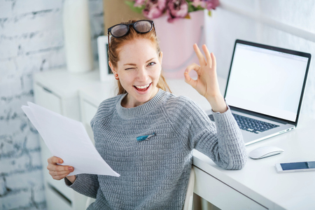 Young beautiful woman with red hair, wearing glasses, working in the office, uses a laptop and mobile phone.の写真素材