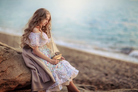 Portrait of a girl near the sea sitting on the rocks with a toy ship in handsの写真素材