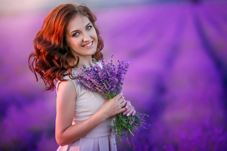 Romantic couple in an endless lavender field at sunset. blond Man and red-haired girl with a bouquet of flowers in love and hugs. French lavender fields.の写真素材