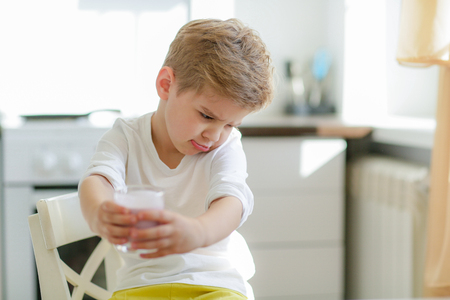 Kid or blonde happy boy eating at table. Childhood and happiness, independence. Breakfast, morning, family. Small boy child eat banana and drink milk. Healthy food and vitamin. dieting, vegetarian.の写真素材