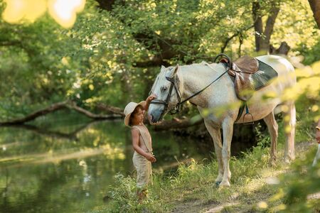 Little baby boy with curly hair dressed as hobbit playing with horse in summer forest.の写真素材