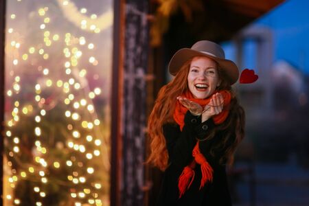 Red hair girl on the background of bright New Years showcases having fun and posing with cardboard hearts in her hands.の写真素材