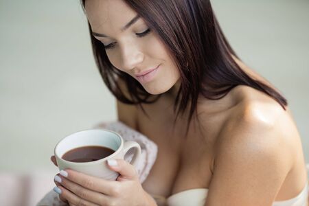 Feminine girl with beautiful smooth hair and bare shoulders holds a cup with a hot drink.の写真素材
