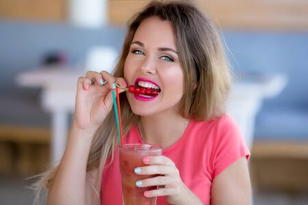 A woman looks at the camera and drinks a cocktail and snacks it with a snack.の写真素材