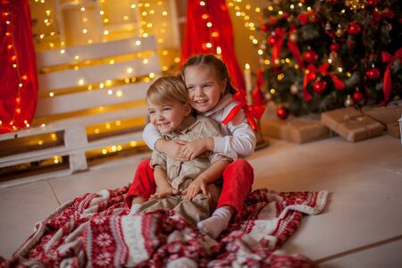 Brother and sister children are photographed and hugged in a room near the Christmas tree at home.の写真素材