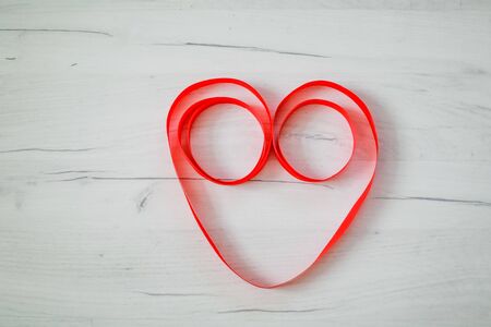 Red heart love symbol from red ribbon on wooden background.