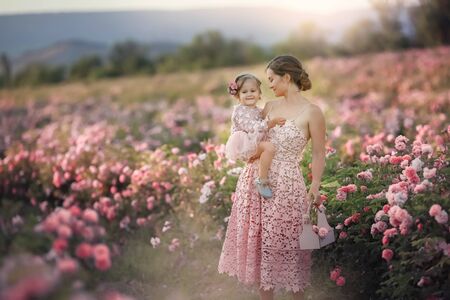 A woman in a retro dress with her daughter 5 years old walking in the spring in a field with roses.の写真素材