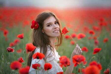 A woman in an agricultural field with a wreath on her head of red poppies.の写真素材