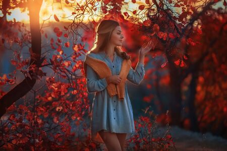 Beautiful girl in autumn garden in trees with red yellow leaves.の写真素材