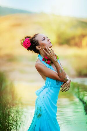 A woman in a stylish blue dress poses in the woods by the lake.の写真素材