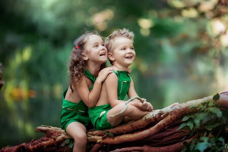 Children a boy and a girl in the forest near a fabulous green lake sitting on a fallen tree.