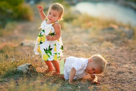 Two baby outdoors a boy and a girl in a dress crawling on the ground.の写真素材