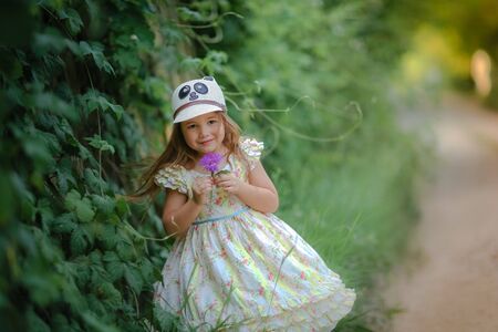 Child girl 5 years stands on the street near the fence braided with green plants.の写真素材