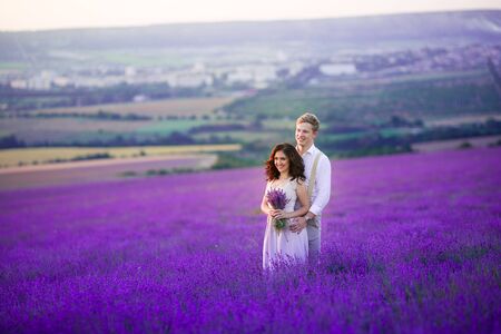 A loving couple standing in a lavender field and hugging. Beautiful bride dressed in luxurious wedding dress. Bride and groom are marriedの写真素材
