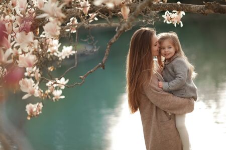 A woman holds a child in her arms against the background of a lake in a garden with magnolia.の写真素材