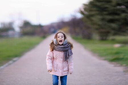 In autumn a girl in a scarf and a warm jacket runs along the sidewalk in the Park.の写真素材