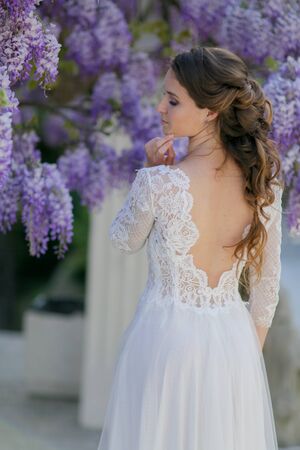 A bride in a wedding dress stands with her back to the camera under a tree.の写真素材