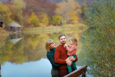 Father mother and child stand on a wooden pontoon on the background of the lake.