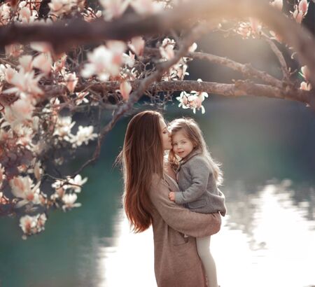 Unrecognizable girl with a child in the background of a lake and a tree. A woman with a daughter in the park.の写真素材