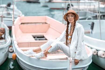 A young girl in a white suit sits on the stern of a pleasure boat.の写真素材