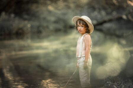 A boy in trousers and without shirts near rivers in the forest with wand in the hands of as if fishermanの写真素材