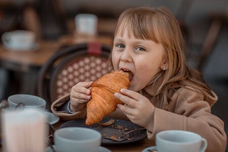 Girl eats croissant in street cafe in autumn.の写真素材