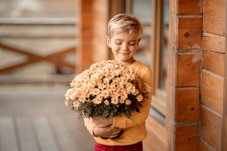 A 7-year-old boy holds a bouquet of flowers near a village wooden house.の写真素材