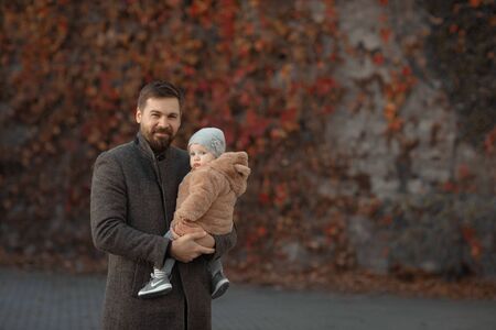 Father holds his daughter in his arms during a walk in the park in the fall.の写真素材