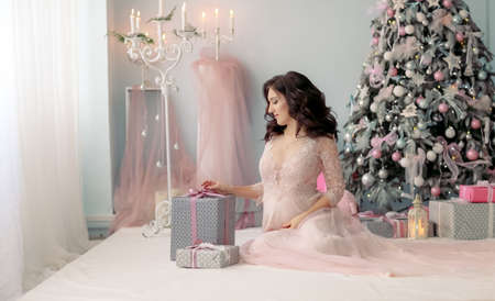 A woman in a long pink wedding dress near a Christmas decorated tree in a bright roomの写真素材