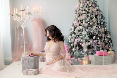 Pregnant woman young girl sitting on the floor of the will of the Christmas tree with a box in her handsの写真素材