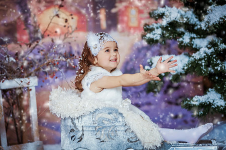 Girl on the background of artificial winter nature in white clothes and winter sledの写真素材