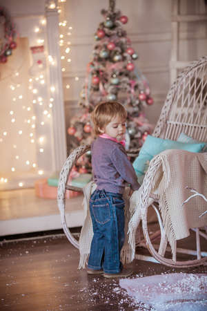 A boy with a pink tie stands near a wheelchair on the background of a Christmas tree and a wall decorated with garlandsの写真素材
