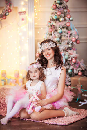 Glamorous mother and daughter dressed in a pink puffy skirt against the background of the Christmas treeの写真素材