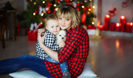 Mother with child in plaid shirts on the background of Christmas red candles and Christmas treeの写真素材