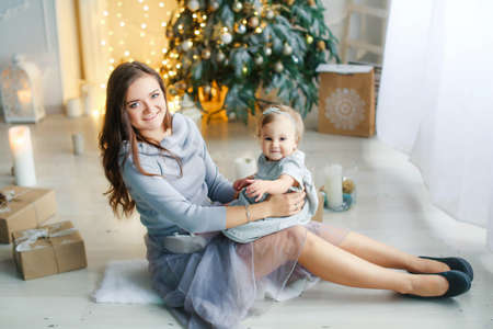 Family of two people mother and daughter 1 year old against the background of the Christmas tree photo in bright colorsの写真素材