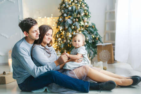 Mom, dad and baby hug and rejoice on Christmas winter evening near the New Year tree.