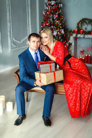 A man gives his beloved woman a gift on new years eve . The man is dressed in an elegant suit and the woman in a long red evening dressの写真素材