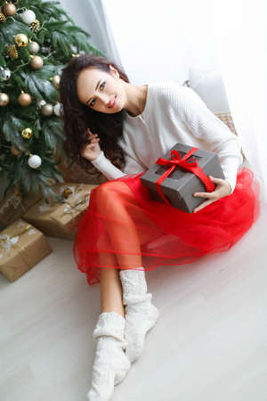 Woman model in a red dress in a photo studio holding a New Years gift in her handsの写真素材