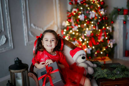 Red Christmas photo of little girl on the sofa with a gift in her handsの写真素材