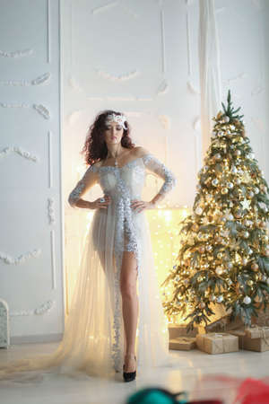 New year photo of a model girl in a white dress on a background of a yellow bright new year treeの写真素材