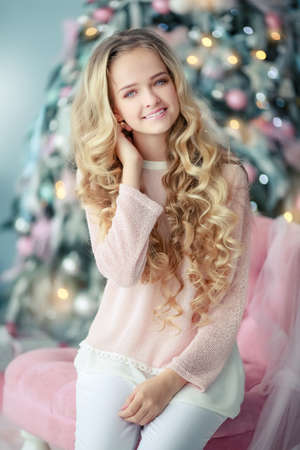 Girl with long blond curly hair on the background of a Christmas tree in the studioの写真素材