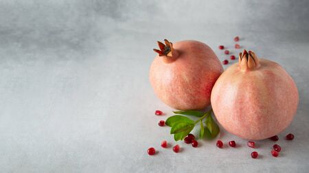 Ripe pink pomegranates fruit with seeds and green leaves on a gray background with copy space. Horizontal orientation.の写真素材