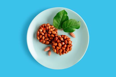 Healthy natural sweetness of kozinaki are prepared from peanuts, honey and molasses, characterized by the presence of antioxidants and fatty acids in its composition, nuts and green leaves on a plate on a blue background. Horizontal orientation. Georgian and Armenian national dishの写真素材