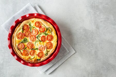 Homemade vegetable pie called quiche with tomatoes, spinach and corn on a gray background with copy space. Flat lay, horizontal orientation.の写真素材