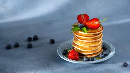 Stack of homemade classic american pancakes with fresh blueberries and strawberries on plate, morning light blue background. Healthy sweet summer breakfast. Horizontal orientation, copy space.の写真素材