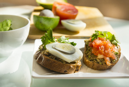 two 2  sandwiches with avocado and tomato and boiled egg on a plate, chopped avocado and tomatoes on...